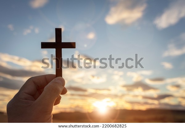 Holding up religious cross\
crucifix to sky at sunset background concept for religion, worship\
and praying