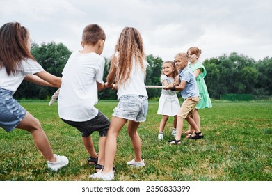 Holding the rope, playing game. Kids are having fun on the field at daytime together. - Powered by Shutterstock