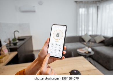 Holding a smartphone with launched security program indoors. Concept of controlling and managing home security from a mobile device