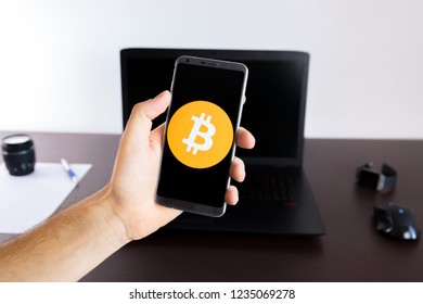 Holding a smartphone on hand with a Bitcoin PNG logo image on screen opened from the Gallery app on the phone covering the whole front display