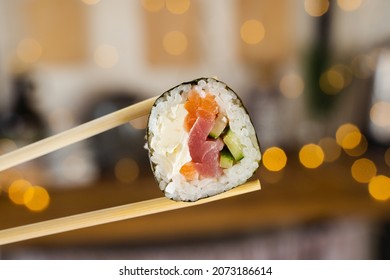 Holding sushi roll on the new year lights background. Christmas decoration. Food delivery at new year eve. Roll with salmon, tuna, cucumber and soft cheese