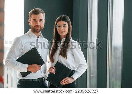 Holding tablet. Man and woman in formal clothes are working together indoors.