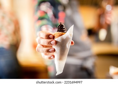 Holding a traditional hungarian stuffed chimney cake dessert in hand with bokeh background