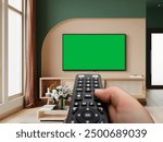 Holding a tv Remote towards Green screen TV .Effortlessly control your entertainment with a sleek remote and green screen TV,