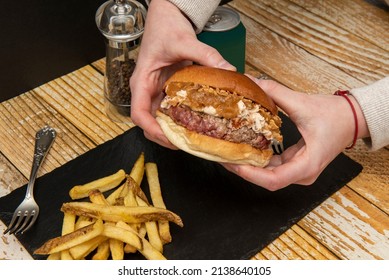 Holding In Two Hands A Beef Burger With Cream Cheese, Crispy And Caramelized Onions