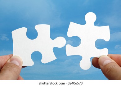 Holding Two Jigsaw Pieces Of A Blank Puzzle Trying To Fit Together Against Blue Sky Background
