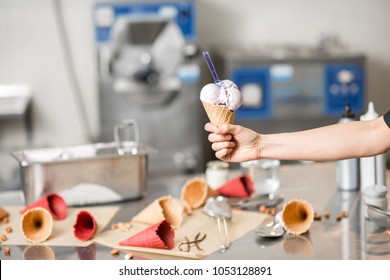 Holding Waffle Cone With Ice Cream At The Kitchen With Food Ingredients And Ice Cream Maker Machine On The Background