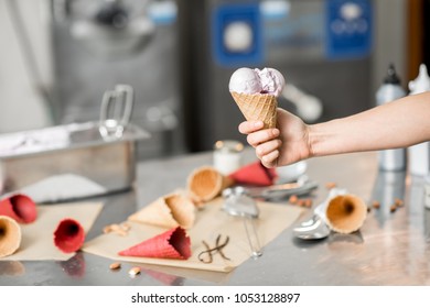 Holding Waffle Cone With Ice Cream At The Kitchen With Food Ingredients And Ice Cream Maker Machine On The Background