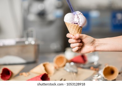 Holding Waffle Cone With Ice Cream At The Kitchen With Food Ingredients And Ice Cream Maker Machine On The Background