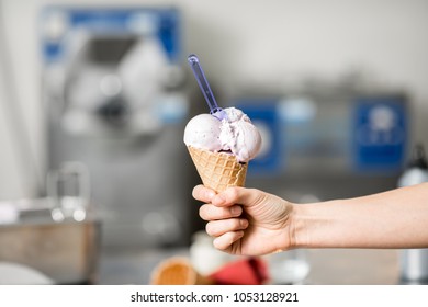 Holding Waffle Cone With Ice Cream At The Kitchen With Food Ingredients And Ice Cream Maker Machine On The Background