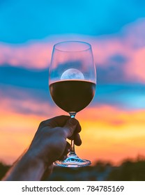 Holding A Wine Glass With Red Wine And Cheers To The Sunset