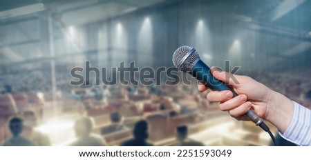 Holds out a microphone speaker on a blurred background.