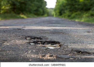 Hole in the asphalt bad condition of the dangerous road surface. Hollow surface in tarmac with a road view in distance. Emergency cover concept. 