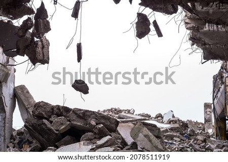 A hole in the body of a building with a pile of construction debris and concrete fragments hanging on the rebar against a uniform gray sky. Background.