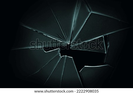 The hole in the broken and cracked glass on black background, closeup 