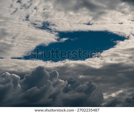 A hole in the clouds reveals a patch of blue sky above, surrounded by dark and ominous clouds.