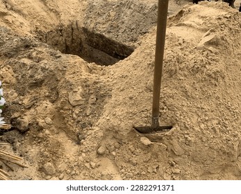 A hole dug in the ground with a shovel nearby. Burial grave dug with a shovel. Place in the sand at the cemetery. - Shutterstock ID 2282291371