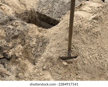 A hole dug in the ground with a shovel nearby. Burial grave dug with a shovel. Place in the sand at the cemetery. - Shutterstock ID 2284917141