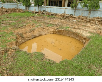 a hole filled with murky water in a grassy field on a construction site