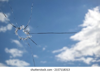 A hole in the glass from a piece of ammunition. window glass pierced by a bullet. broken glass. blue sky on the background. Horizontal image.