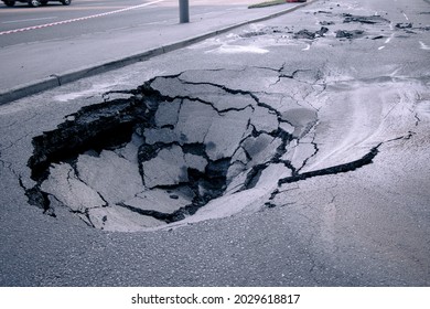 A hole in the ground in the middle of the road. A large pit in the asphalt due to a pipeline accident