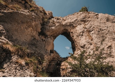 Hole in old rock with trees, grass, flowers and blue sky view. Natural attraction of Balkans. Dupni kamen is tourist landmark of Stara planina mountain range. Serbian natural site in Balkan Mountains.
