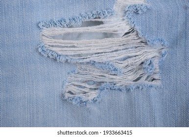 Hole In An Old Torn Blue Jeans Showing The Frayed Threads And Fabric Texture

