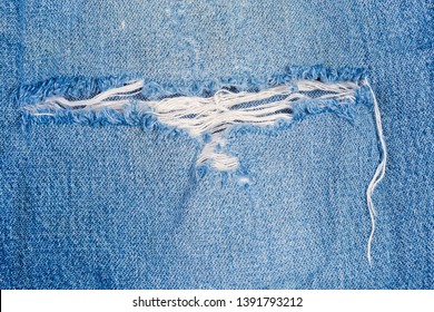 Hole on blue  jeans. Texture of the old torn denim showing the frayed threads, fragment close-up 