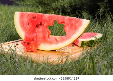 a hole in the shape of a six-pointed star is cut in a slice of watermelon, which lies on a wooden board on a green lawn