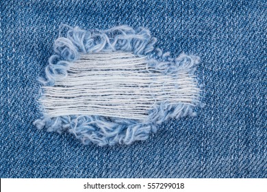 Hole And Threads On Denim Jeans. Ripped Destroyed Torn Blue Jeans Background. Close Up Blue Jean Texture 