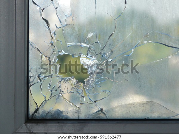 ウィンドウガラスの穴 穴の周りに広がる亀裂 緑の木の葉がガラスにぼやけている 汚い窓枠 内側から通りが見える の写真素材 今すぐ編集