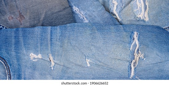 Hole and worn places in the different old torn jeans showing the frayed threads and fabric texture, fragment, panoramic view 