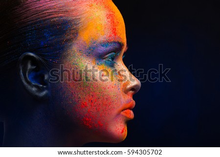 Holi festival of colors background. Female face art with creative make up. Closeup cropped studio portrait of young fashion model with bright colorful mix of paint. Profile on black with copy space