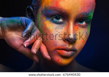 Holi festival of colors background. Female face art with creative make up. Closeup cropped studio portrait of young fashion model with bright body art