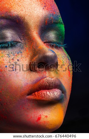 Holi festival of colors background. Female face art with creative make up. Closeup cropped studio portrait of young fashion model with bright body art