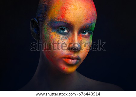 Holi festival of colors background. Female face art with creative make up. Closeup cropped studio portrait of young fashion model on black with copy space
