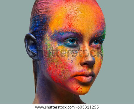Holi festival of colors. Female face art with creative make up. Closeup studio portrait of young fashion model isolated on gray background with bright colorful mix of paint