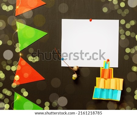 Holiday background with white sheet, paper flags and light garland on black chalkboard with bokeh effect. Holiday school composition with copy space suitable for teachers day, birthday or 1 september