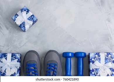 Holiday christmas birthday party sport flat lay composition with gray shoes, blue dumbbells and blue gifts on gray concrete background. Top view, horizontal orientation