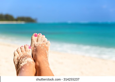 Holiday concept. Woman feet close-up relaxing on beach, enjoying sun and splendid view 