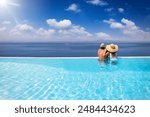 A holiday couple in a big infinity pool enjoys the panoramic view to the blue sea during summer vacation time