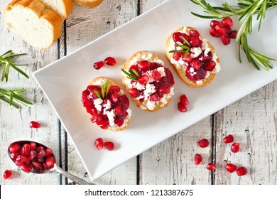 Holiday Crostini Appetizers With Cranberries, Pomegranates And Feta Cheese. Above View On A Serving Plate Over A White Wood Background.