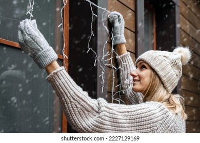 holiday decorations. woman install electric christmas string lights on house exterior facade - Powered by Shutterstock