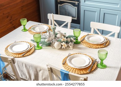 Holiday dining table is elegantly arranged with green glassware, woven placemats and white plates, creating warm and inviting setting on modern kitchen background. Christmas and New Year celebration - Powered by Shutterstock