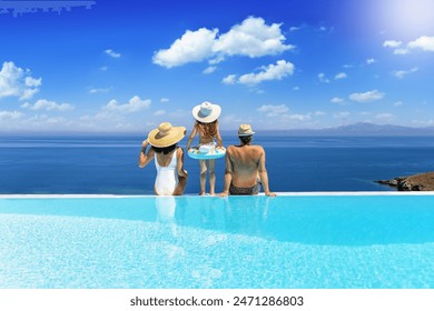 A holiday family sits at the edge of an infinity pool and enjoys the summer day view of the mediterranean sea - Powered by Shutterstock