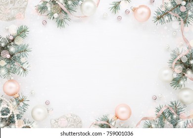 Holiday frame of Christmas decorations on white background with fir branch, pink balls, ribbon and pearls. Elegant New Year`s snowy card. Top view.
