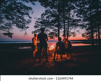 Holiday with friends in nature. Group of young people near camp fire , telling stories near the fire with wood, flames in the nature at night near lake. - Powered by Shutterstock