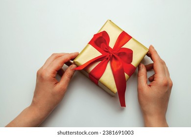 A holiday gift. Box in a gold gift wrapping with a red bow, on a white background. Merry Christmas, Happy New Year and Valentine's Day greetings. Postcard. High quality photo - Powered by Shutterstock