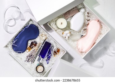 Holiday gift boxes. White gift boxes with sleep care set for men and women. Preparing self care package, craft gift box with mask for sleep, aroma candle, aroma sticks, oil and bubble bath. Flat lay