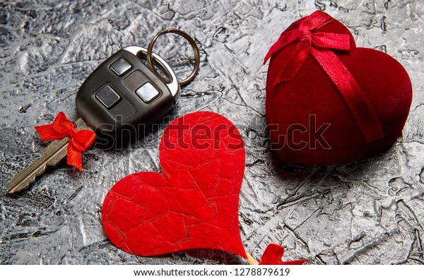 \
Holiday gift jewels in a box in the form of a\
heart with a bow and a car key with a red bow on a gray background.\
Valentine\'s Day.